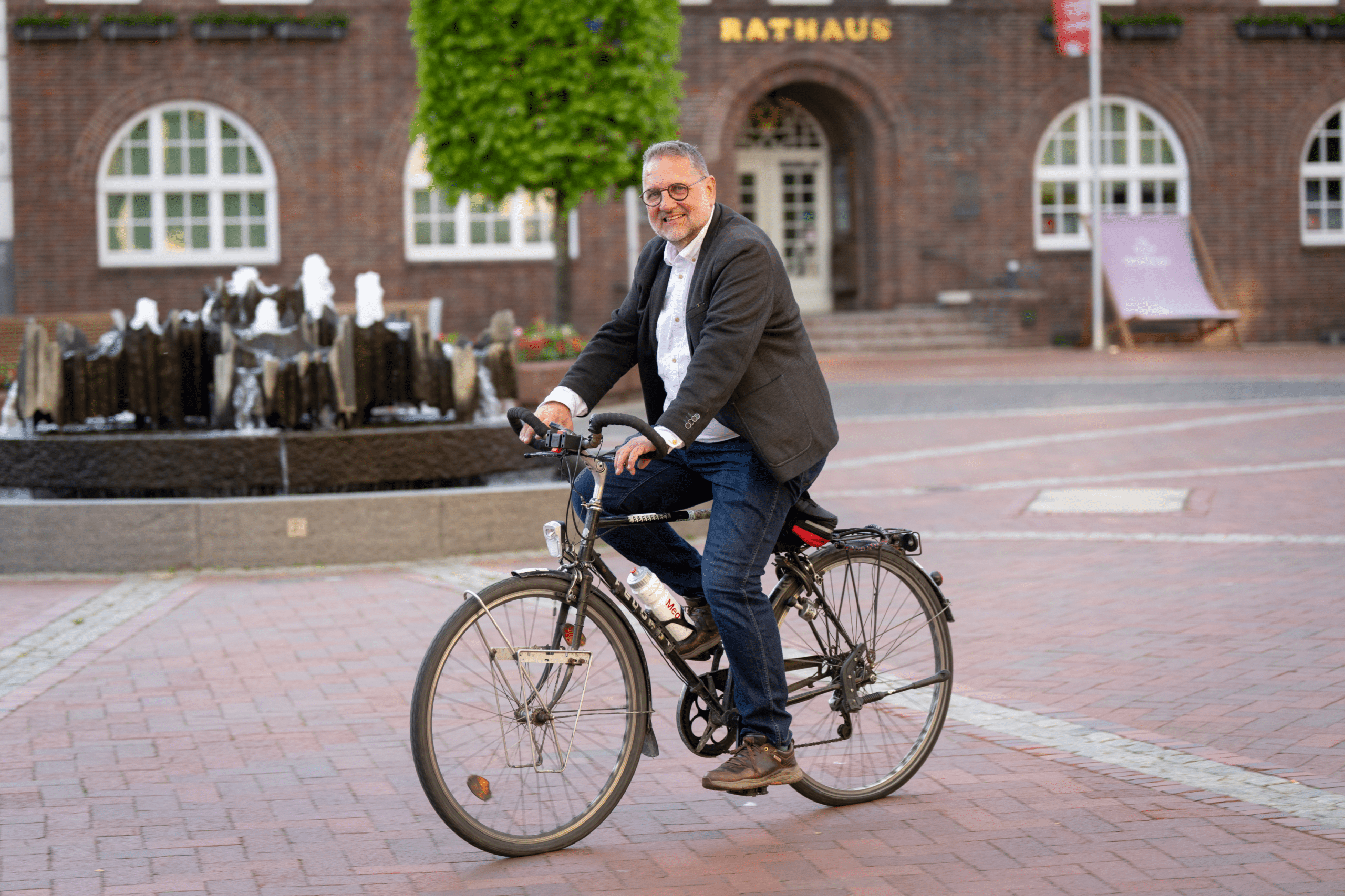 Peter Meiwald fährt lächelnd mit dem Fahrrad über den Westersteder Marktplatz.